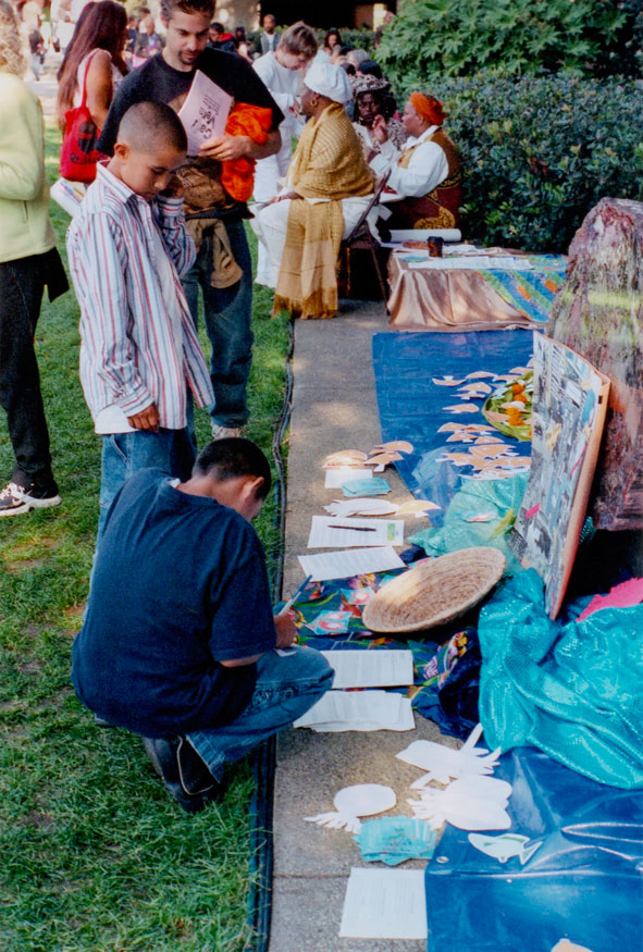 visitors writing prayers on paper fish to add to the altar